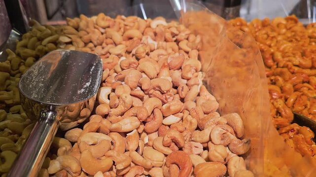 Self serve nut bar with cashews, peanuts, almonds, and seasoned mixes arranged in divided bins, with metal scoops, warm shop lighting, and fresh gourmet snack display.