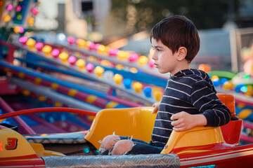 Little boy looking away while riding a colorful carousel car at sunset © Oleksii Yemelianov