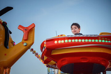 Child looking forward in illuminated red carousel vehicle at evening funfair © Oleksii Yemelianov