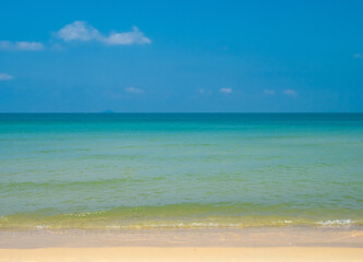 Fototapeta premium Beautiful tropical sandy beach with crystal clear turquoise water and a soft white wave splashing onto the shore under a vibrant blue sky during a sunny summer day.