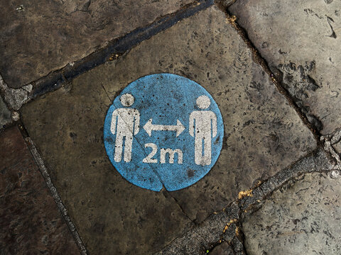 Social distancing 2m floor sticker on stone pavement in Liverpool, UK indicating public health safety for pedestrians and urban street guidance