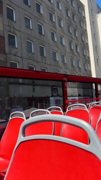 Passengers enjoy panoramic views from upper deck of double-decker bus in bustling city center. Urban exploration and sightseeing concept. Bright red seating adds vibrancy to travel experience