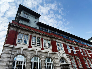 Obraz premium Historic red brick post office building with modern rooftop extension in Manchester, UK, urban architecture and ornate stone facade under a blue cloudy sky
