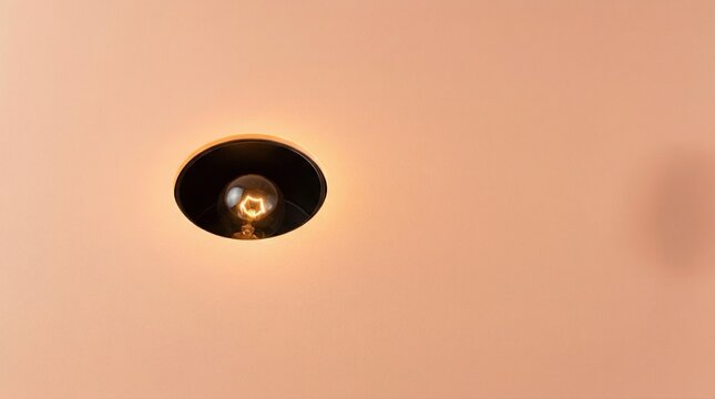 Minimalist Concept of an Illuminated Lightbulb Shining Through a Circular Hole in a Smooth Peach Colored Background