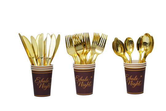 Gold plastic cutlery in paper cups. Disposable party tableware for festive events.