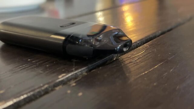 Vape pen on wooden surface with blurred reflections, suitable as product background and copy space