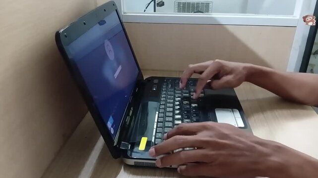 Close-up footage of hands typing on a laptop keyboard on a wooden desk.