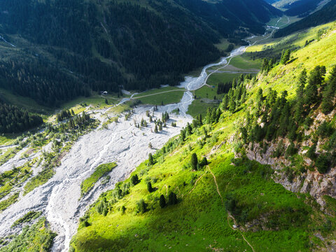 The river winds gracefully through a vibrant green valley, surrounded by lush vegetation and the enchanting Alps in the background