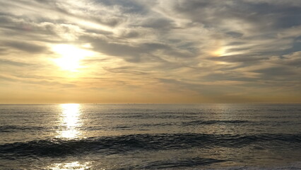 Obraz premium Dramatic Cloudy Sky with Bright Sun Reflecting on Ocean. Dramatic clouds filled with morning sunlight over a calm ocean seascape in Gangneung, showing bright sun reflection on gentle waves.