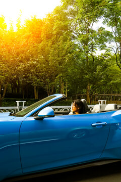 An Asian woman drives a blue convertible sports car down the street.