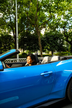 An Asian woman drives a blue convertible sports car down the street.