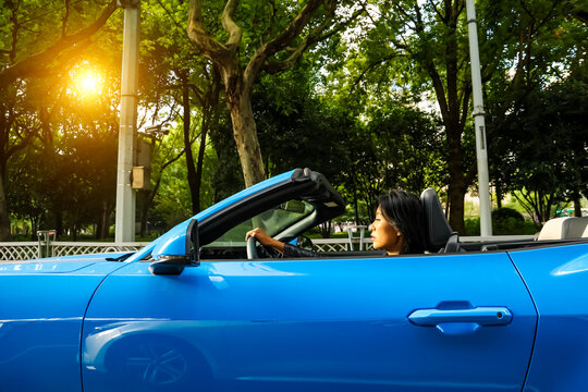 An Asian woman drives a blue convertible sports car down the street.