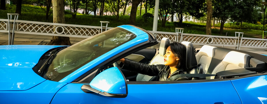 An Asian woman drives a blue convertible sports car down the street.