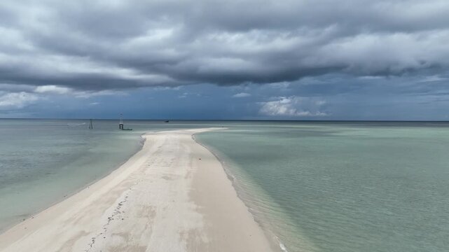 A pristine, deserted sandbank island glows in the middle of crystal clear turquoise tropical waters under a vibrant blue sky. Aerial drone view of this natural sand formation, a perfect remote paradis