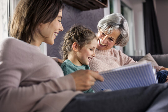 Daughter looking at photo album while sitting by family in living room
