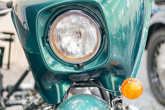 A side profile view of a dark green, well-maintained vintage motorcycle with chrome accents, featuring a round metal headlight and a turn signal light Exhaust pipe visible along the side