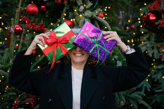 Smiling woman hiding face with wrapped gift by decorated tree