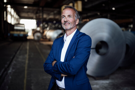 Thoughtful businessman with arms crossed standing at metal industry
