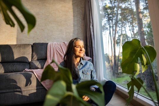 Smiling mature woman looking out of window at home