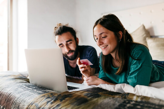 Happy couple lying on bed shopping online