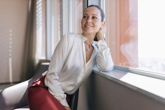 Smiling mature businesswoman leaning on window sill in office