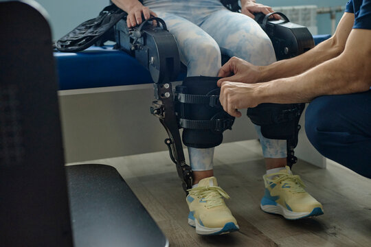 Male therapist adjusts exoskeleton on woman's leg in clinic