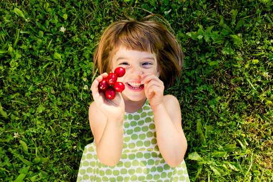 Smiling little girl with cherries lying on a meadow