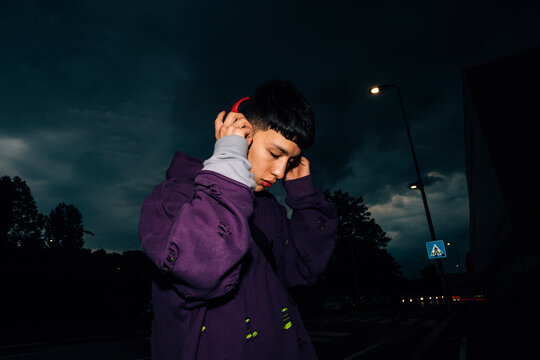 Young man with eyes closed listening music through headphones at night