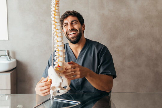 Happy young physiotherapist with human spine model at medical clinic