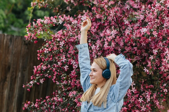 Smiling woman enjoys music near a blooming pink tree outdoors