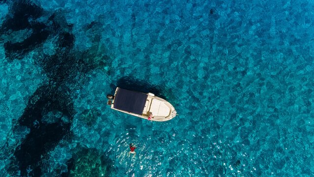 Woman swims near a motorboat in the clear turquoise sea of Sardinia