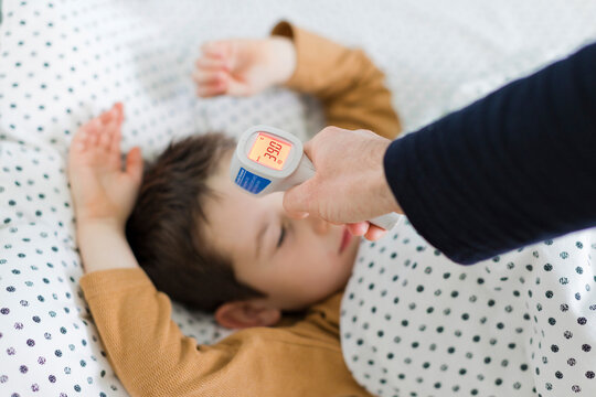 Hand of father measuring temperature of son lying on bed at home