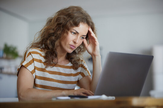 Woman sitting with head in hands while working on laptop at home