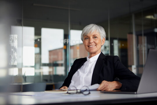 Portrait of smiling senior businesswoman sitting at desk in office