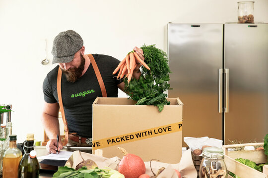 Mature man with delivery service packing organic vegetables in cardboard