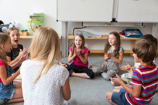 Teacher and pupils sitting on floor of their classroom singing and clapping hands