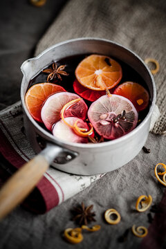 A saucepan contains hot mulled wine with orange and lemon indoors