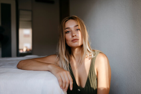 Seductive young woman sitting by bed in bedroom at home