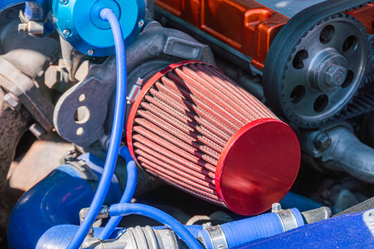 Close-up view of high-performance air intake system featuring cylindrical red filter, blue intake pipe, and intricate mechanical details, emphasizing vibrant colors and natural lighting in outdoor