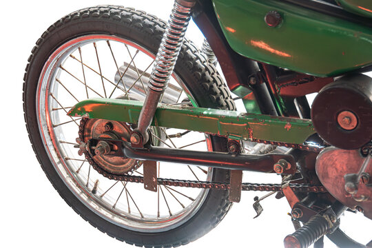 Rusted vintage motorcycle rear view, featuring knobby tire and exposed metal parts, showcasing worn chain and spring suspension against plain white backdrop