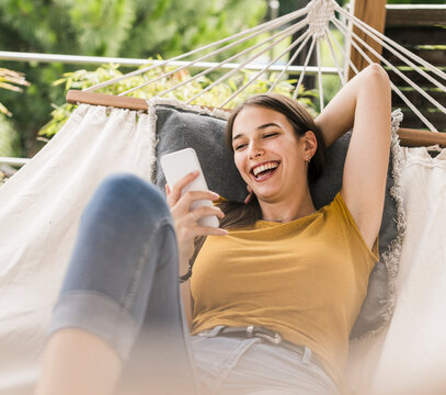 Cheerful beautiful woman using mobile phone while resting on hammock