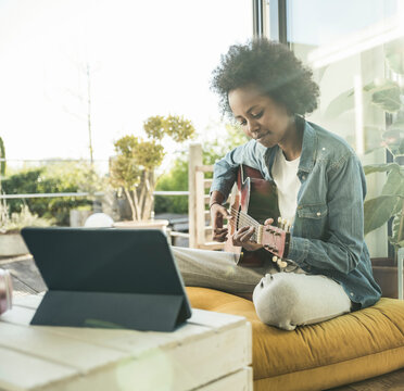 Woman practicing guitar through e-learning on digital tablet at home