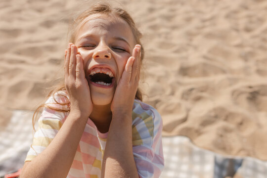 A happy girl shows a toothless smile on the sandy beach