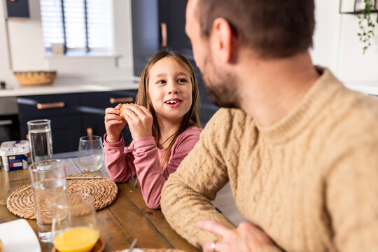 Happy girl having breakfast with father sitting in kitchen