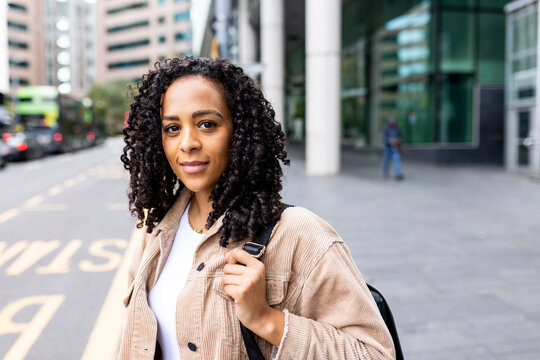 Smiling woman with curly hair on footpath at bus stop