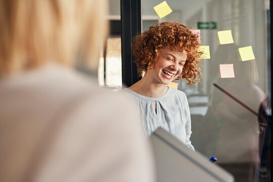 Laughing businesswoman with sticky notes at glass pane in office