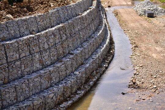 Retaining wall constructed from gabion baskets filled with stones viewed from the side outdoors, Gabion retaining wall