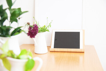 Fototapeta premium Black tablet mockup surrounded by green plants and purple flower