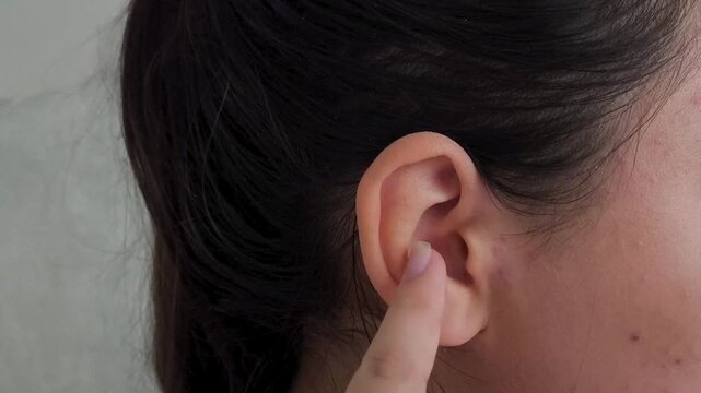 A woman cleans her ear with her finger. Woman touching ear with finger, ear discomfort, ear hygiene, otolaryngology and healthcare concept.