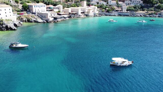 Drone footage of traditional fishing boats floating in the crystal-clear turquoise waters of Limeni Bay, Mani, Greece, with historic stone buildings along the Mediterranean coastline